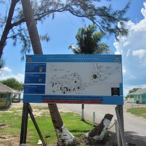 A view of a sign board detailing the Garvin Park Dock Extension and New Ramp, surrounded by trees with a glimpse of nearby structures.