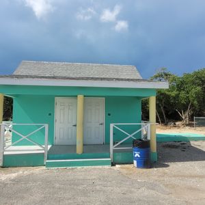 A turquoise building with two doors and a yellow roof, surrounded by greenery and a playground.