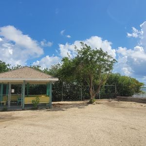 A gazebo by the water surrounded by greenery and blue skies with clouds.