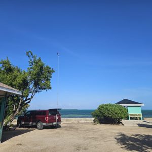 A setup at a coastal park with a truck and a radio antenna, featuring clear skies and water in the background.