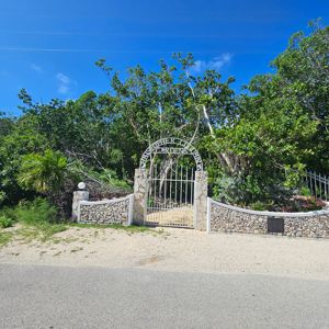 A gated entrance to Christopher Columbus Gardens, surrounded by greenery and under a clear blue sky.