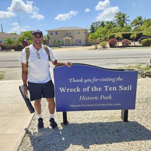 An operator stands next to a sign for the Wreck of the Ten Sail Historic Park in Grand Cayman.