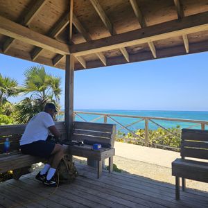 An operator setting up equipment at a shaded gazebo overlooking the ocean.