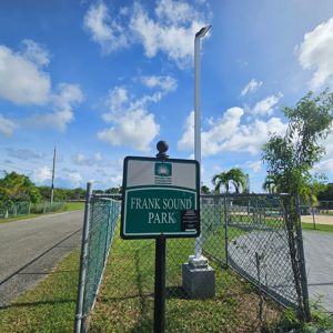 A sign indicating Frank Sound Park with a clear blue sky and some greenery in the background.