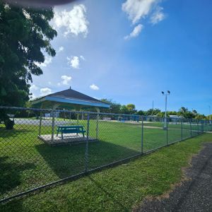 A grassy area with a gazebo and a picnic table, enclosed by a chain-link fence.