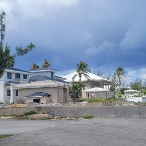 A coastal view with several buildings and palm trees, under a partly cloudy sky.