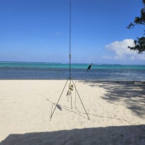 A radio antenna set up on a sandy beach with a clear blue sky and ocean in the background.