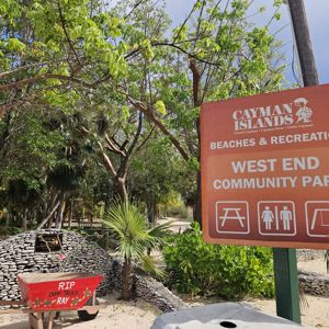 A park sign indicating West End Community Park in the Cayman Islands, surrounded by trees and a scenic environment.