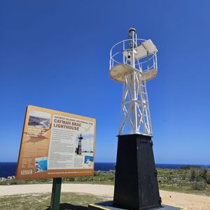 A lighthouse with a sign describing the historical significance of Cayman Brac Lighthouse under a clear blue sky.