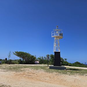 An outdoor area featuring a tall white structure resembling a lighthouse, surrounded by greenery and a clear blue sky.