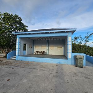 A blue structure with a picnic table in front, surrounded by trees and a clear sky.