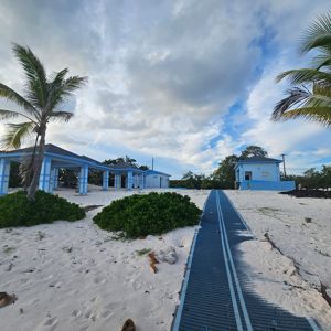 A scenic view of blue buildings set against a sandy beach with palm trees under a cloudy sky.