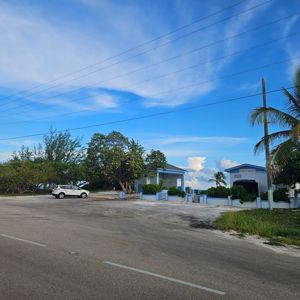 A view of a public beach area with a parking space, buildings, and trees under a clear blue sky.
