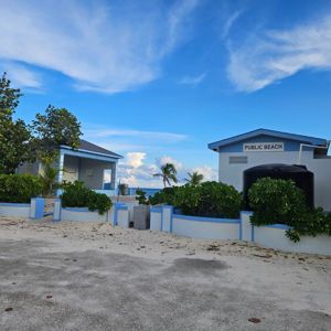 View of a public beach area with structures and greenery against a blue sky.