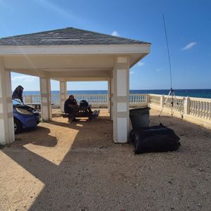 Operators working under a shelter near the beach with a car parked nearby and antennas set up.