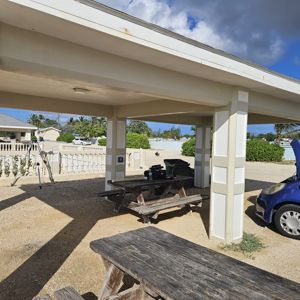 A shaded picnic area with a wooden table and a blue car parked nearby, showcasing a pleasant location for outdoor activities.