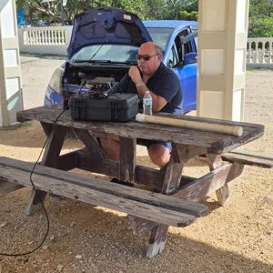 Operator set up at a picnic table with radio gear, working from a shaded area under a structure.