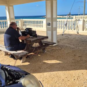 An operator using radio equipment at a beachside location under a shelter.
