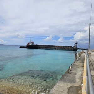 A tugboat near the shore with clear blue water and a coastal road