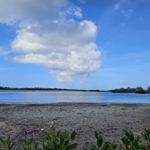 A scenic view of a coastal area with a blue sky, clouds, and water in the foreground.