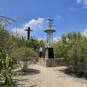 A person standing beside a communication tower surrounded by sparse vegetation under a clear blue sky.