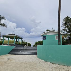 A gazebo near the beach with palm trees and a small building in the background.