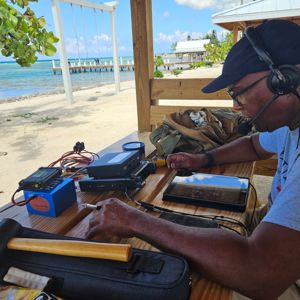 An operator set up at a wooden table by the beach, using a radio and tablet for activation.
