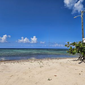 A sandy beach with clear blue water and some clouds in the sky, featuring a radio antenna.