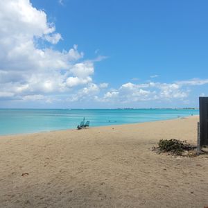 A scenic beach view with sand, palm trees, and the ocean under a partly cloudy sky.