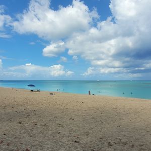 A scenic beach view with soft sand and turquoise water under a partly cloudy sky.