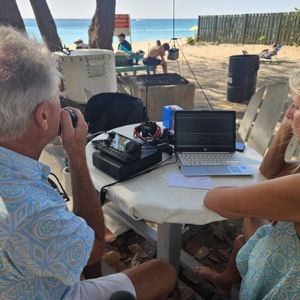 Operators engaging in radio communication at a beachside location with visible ocean and sand in the background.