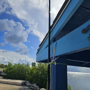 A view of a blue structure with a radio antenna by the water under a partially cloudy sky.