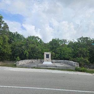 A stone monument surrounded by greenery near a roadside.