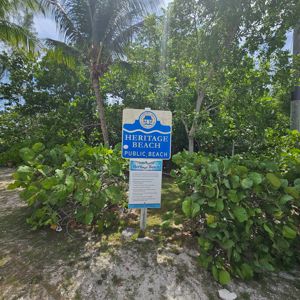 A sign indicating 'Heritage Beach Public Beach' surrounded by lush greenery.
