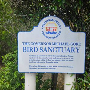 A sign indicating the Governor Michael Gore Bird Sanctuary in the Cayman Islands, surrounded by greenery.